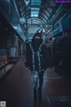 A woman in a black jacket and mask walking down a street.